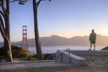 A man overlooks the Golden Gate Bridge with mountains in the background.